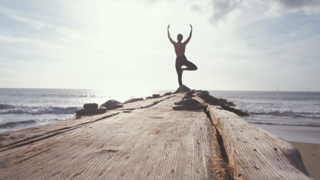 Frau mach Yoga am Ende eines Stegs mit Blick auf das Meer